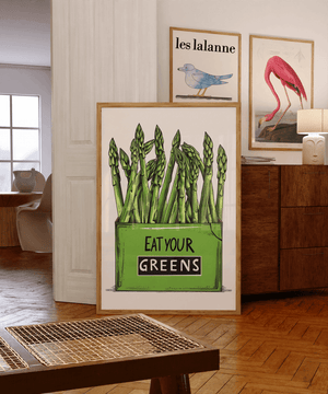 Køkkenplakat med grønne asparges og teksten "Eat Your Greens" i en træramme – sjov og farverig vægdekoration til køkkenet.