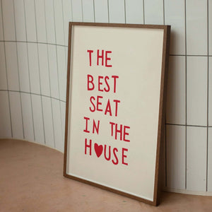 Plakat med rød tekst “The Best Seat in the House” og hjerte – humoristisk vægkunst til badeværelse eller gæstetoilet, indrammet og opstillet i moderne interiør.