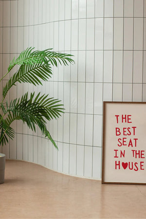 Plakat med rød tekst “The Best Seat in the House” og hjerte – humoristisk vægkunst til badeværelse eller gæstetoilet, indrammet og opstillet i moderne interiør.